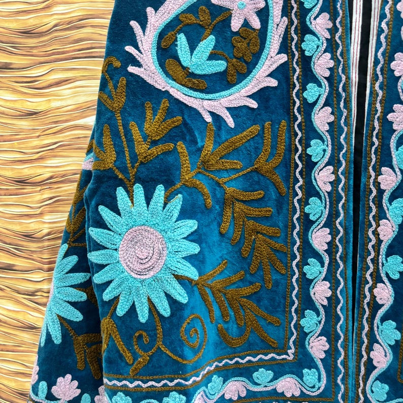 K&ouml;nnte beinhalten: T&uuml;rkisblaue Samtjacke mit aufwendiger Blumenstickerei in Hellblau, Braun und Rosa. Die Jacke zeigt ein detailliertes Muster aus Blumen und Bl&auml;ttern, mit einem kontrastierenden schwarzen Futter an den R&auml;ndern.
