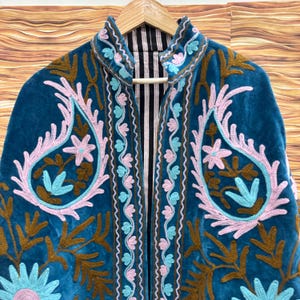 K&ouml;nnte beinhalten: T&uuml;rkisblaue Samtjacke mit aufwendigen Stickereien in Rosa, Hellblau und Braun. Die Jacke hat ein Paisley-Design und florale Muster. Das Innenfutter ist schwarz-wei&szlig; gestreift.