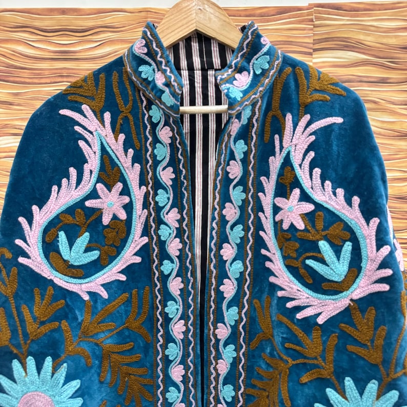 K&ouml;nnte beinhalten: T&uuml;rkisblaue Samtjacke mit aufwendigen Stickereien in Rosa, Hellblau und Braun. Die Jacke hat ein Paisley-Design und florale Muster. Das Innenfutter ist schwarz-wei&szlig; gestreift.