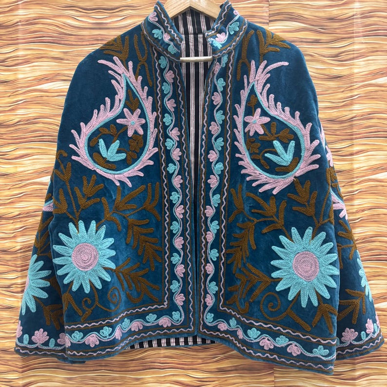 K&ouml;nnte beinhalten: T&uuml;rkisblaue Samtjacke mit aufwendiger Blumenstickerei in Rosa, Braun und Hellblau. Die offene Jacke hat ein Paisley-Design und ein gestreiftes Futter, das einen Bohemian-Look zeigt.