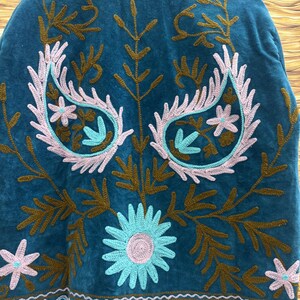 K&ouml;nnte beinhalten: T&uuml;rkisfarbener bestickter Stoff mit floralem und Paisley-Design. Die Stickerei verwendet hellrosa, t&uuml;rkis und braunes Garn. Das Design umfasst Paisley-Formen, Blumen und Blattmuster. Der Stoff hat eine weiche, samtige Textur.