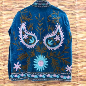 K&ouml;nnte beinhalten: T&uuml;rkisfarbene Jacke mit aufwendiger Stickerei. Die R&uuml;ckseite zeigt ein gro&szlig;es Blumenmuster mit Paisley-Elementen in Rosa, Braun und T&uuml;rkis. Die Jacke hat einen hohen Kragen und einen detaillierten Besatz.