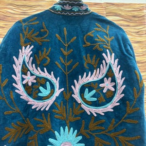 K&ouml;nnte beinhalten: T&uuml;rkisfarbene Jacke mit aufwendiger Stickerei. Das Design zeigt florale und Paisley-Muster in Rosa, Braun und T&uuml;rkis. Kragen und Kanten sind ebenfalls bestickt. Die Jacke ist aus weichem, samtigem Material gefertigt.
