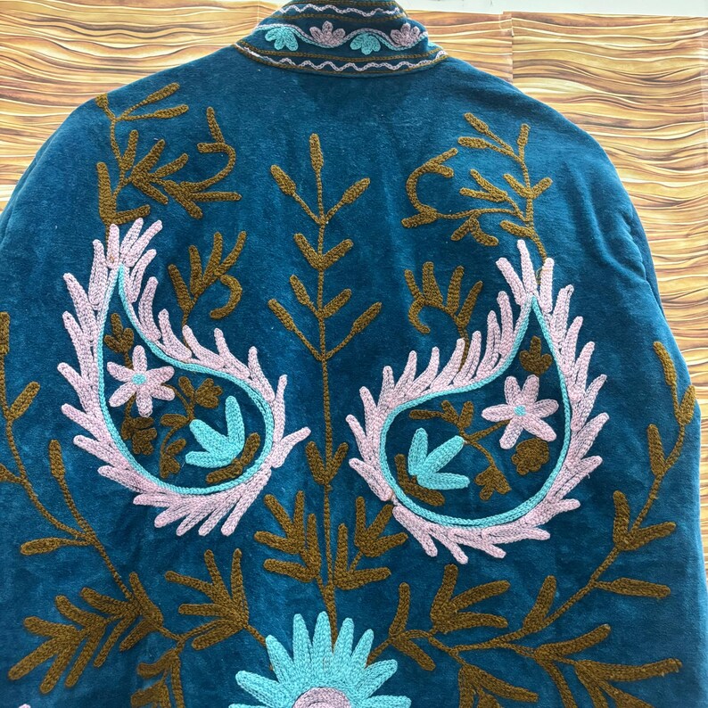 K&ouml;nnte beinhalten: T&uuml;rkisfarbene Jacke mit aufwendiger Stickerei. Das Design zeigt florale und Paisley-Muster in Rosa, Braun und T&uuml;rkis. Kragen und Kanten sind ebenfalls bestickt. Die Jacke ist aus weichem, samtigem Material gefertigt.