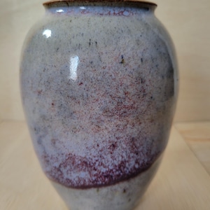 May include: A white ceramic mug with a black handle and the text "But First, Coffee" in a black, bold font. The mug is sitting on a wooden surface. The mug is approximately 4 inches tall.
