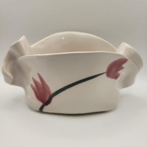 May include: A white ceramic mug with a black handle and the text "But First, Coffee" in a bold, black font. The mug is set against a blurred background, suggesting a cozy setting.