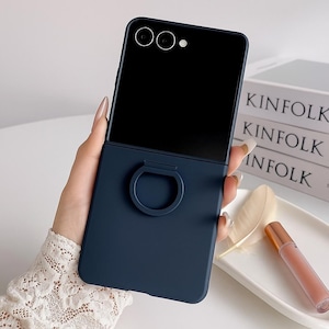 May include: A navy blue phone case with a built-in ring holder. The case is designed to fit a smartphone, with cutouts for the camera and screen. The ring holder is a circular design. The phone case is shown against a neutral background.