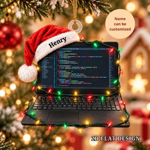Könnte beinhalten: Ein flaches, zweidimensionales Ornament in Form eines Laptops, das Computercode auf dem Bildschirm anzeigt. Eine rot-weiße Weihnachtsmannmütze mit dem Namen Henry auf dem Rand liegt auf dem Laptop, der mit einer Lichterkette umwickelt ist.
