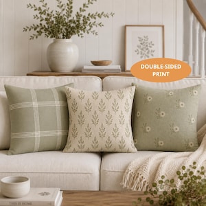 May include: Three square throw pillows arranged on a sofa. The left pillow is sage green with a white grid pattern. The center pillow is cream with a repeating green leaf print. The right pillow is sage green with a small white floral pattern.