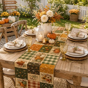 May include: A wooden dining table set for a meal with a patchwork table runner featuring autumn-themed patterns of pumpkins, leaves, and plaid. The table includes white plates, beige napkins with decorative rings, and amber-colored glassware.