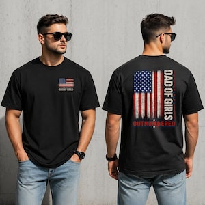May include: A black short-sleeved t-shirt featuring a small American flag graphic with the text DAD OF GIRLS on the left chest and a large distressed American flag graphic on the back with the text DAD OF GIRLS OUTNUMBERED in white and red.