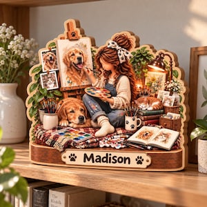 May include: A multi-layered wooden display featuring a person painting a golden retriever on an easel. The scene includes a dog, a cat, art supplies, and a plaque with the name Madison and paw prints. The design incorporates various pet portraits.