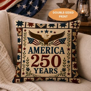 May include: Square throw pillow with a patriotic design. The pillow features an eagle, American flags, and the text "AMERICA 250 YEARS" in red and blue. The border has a patchwork pattern with stars.