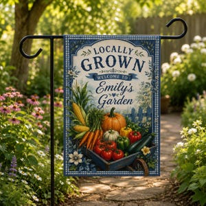 May include: A rectangular garden flag featuring a blue and white gingham border and the text LOCALLY GROWN WELCOME TO Emily's Garden. The illustration depicts a blue wheelbarrow filled with corn, carrots, tomatoes, peppers, and a pumpkin.