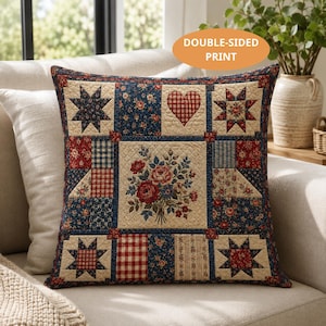 May include: Square decorative pillow with a patchwork design. The pillow features a floral bouquet, stars, and a heart in a mix of red, blue, and cream fabrics. The pillow is on a cream-colored sofa. The text "DOUBLE-SIDED PRINT" is in an orange oval.