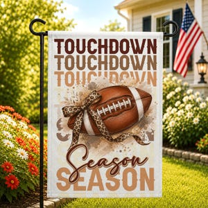 May include: A rectangular garden flag featuring the repeated text TOUCHDOWN in brown and tan, a central brown football with white laces wrapped in a leopard print ribbon, and the word Season in brown script above the repeated text SEASON in tan.