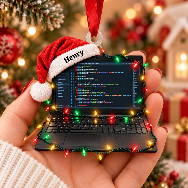 May include: A miniature black laptop ornament featuring a red Santa hat with the name Henry printed on the white trim. The screen displays lines of computer code, and the device is wrapped in a string of small, colourful Christmas lights.