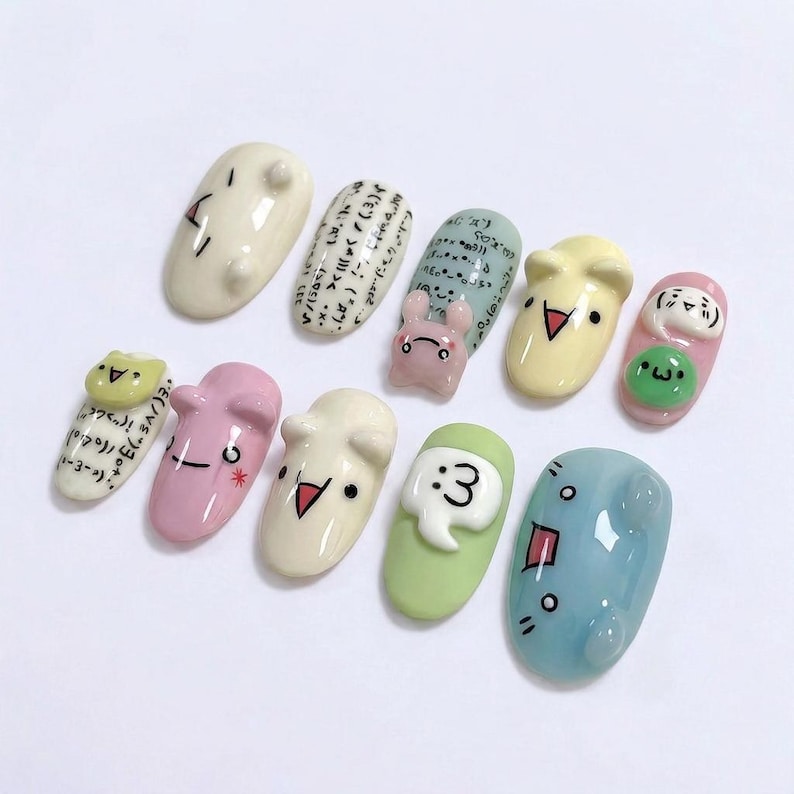 May include: A set of ten decorative nail art designs. Each nail showcases a unique design, including cartoon faces, mathematical symbols, and a small bunny. The nails are painted in pastel shades of pink, green, and blue.
