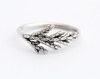 May include: A silver ring with a detailed design of a cedar branch.