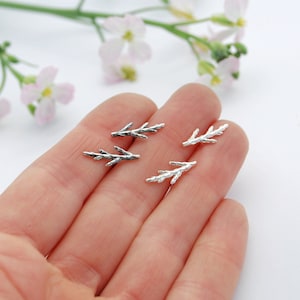 May include: A pair of silver earrings shaped like delicate branches. The earrings are small and dainty, perfect for everyday wear.