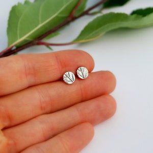 Puede incluir: Un par de pendientes de bot&oacute;n de plata con un dise&ntilde;o de hoja texturizada.