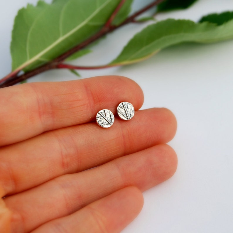 Puede incluir: Un par de pendientes de bot&oacute;n de plata con un dise&ntilde;o de hoja texturizada.