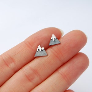 May include: A pair of silver mountain-shaped stud earrings with white enamel accents.