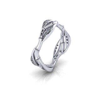 May include: A silver-toned ring featuring a textured bamboo-inspired design. The band is composed of segmented nodes and internodes, with small, clear, sparkling stones embedded along specific sections of the metallic surface, creating a reflective finish.