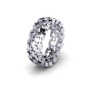 May include: A silver-toned ring featuring an intricate, openwork design composed of repeating puzzle piece shapes. The band has a continuous, cut-out pattern that creates a lattice effect around the entire circumference of the circular metal ring.