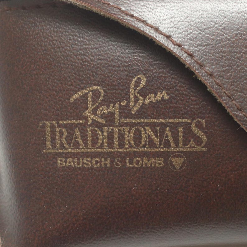 May include: Close-up of a brown leather case with the Ray-Ban logo and the text "TRADITIONALS" in gold lettering. The case also features the "BAUSCH & LOMB" brand name.