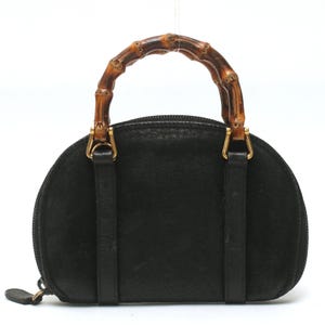 May include: A black semi-circular handbag featuring a textured surface and a curved bamboo handle. The bag includes gold-toned metal hardware connecting the handle to the body, a top zipper closure, and two vertical leather straps on the front.