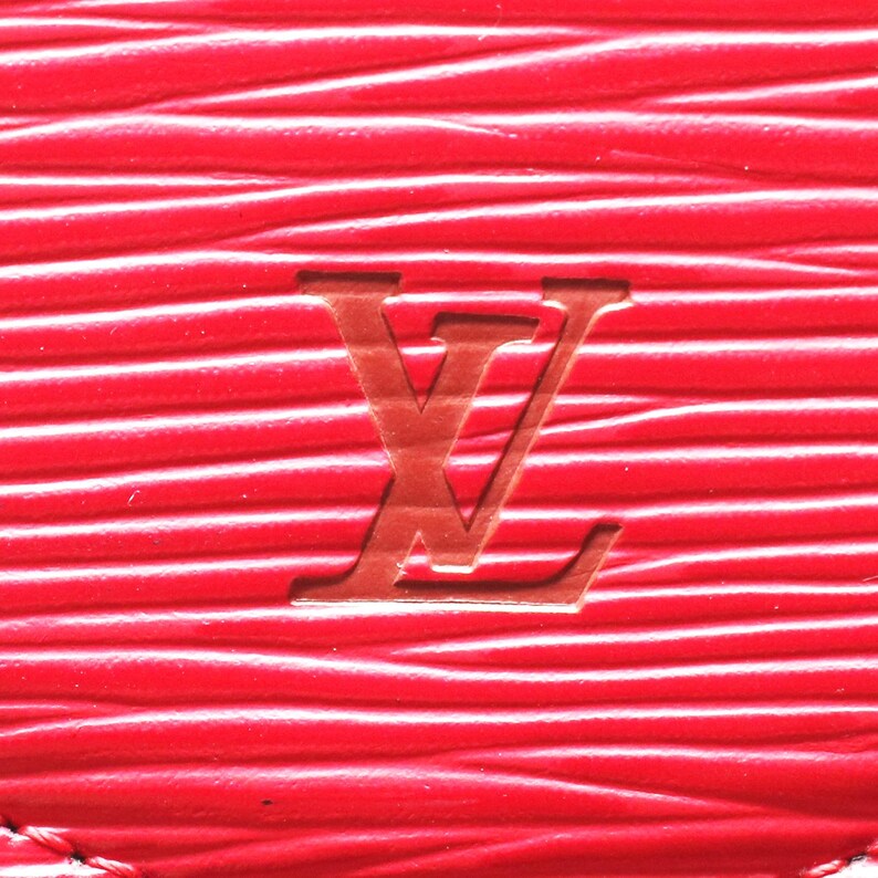 May include: A bright red leather surface featuring a distinct horizontal wavy texture and a debossed Louis Vuitton logo centered in the middle. The material displays a consistent grain pattern with deep grooves running across the entire frame.