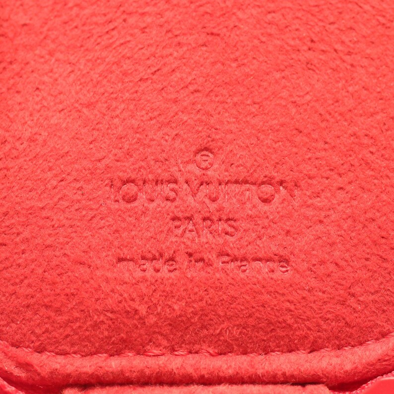 May include: A bright red textured material featuring an embossed logo that reads LOUIS VUITTON PARIS made in France. The surface has a soft, felt-like appearance with a consistent vibrant red color throughout the entire visible area of the item.