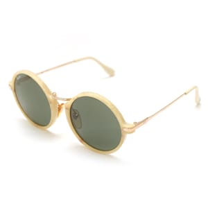May include: Oval-shaped sunglasses with a light beige frame and dark green lenses. The frames are connected by a thin gold-colored bridge and arms. The sunglasses are angled slightly, showcasing their design.