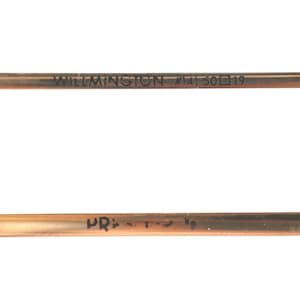 May include: Close-up of a copper-colored metal rod with the text "WILMINGTON #14) 50 19" printed on it. The rod has a slightly curved shape and appears to be a component of a larger item. The background is plain white.