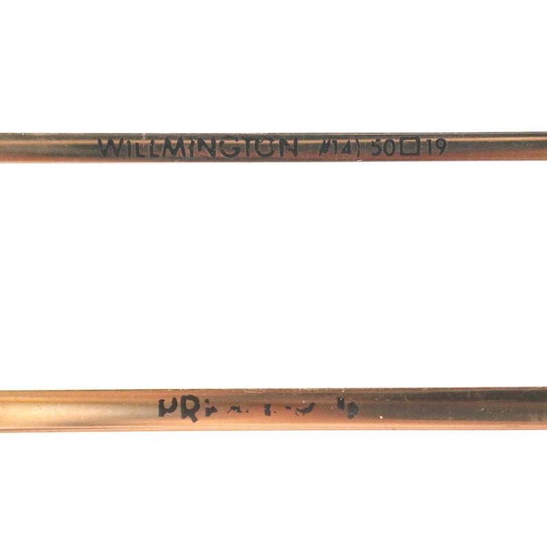May include: Close-up of a copper-colored metal rod with the text "WILMINGTON #14) 50 19" printed on it. The rod has a slightly curved shape and appears to be a component of a larger item. The background is plain white.