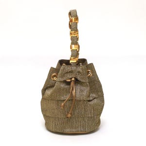 May include: A metallic gold bucket bag with a textured fabric finish, featuring a drawstring closure with gold-tone metal eyelets and a decorative gold-tone chain link handle. The bag has a rounded base and a structured, gathered top opening.