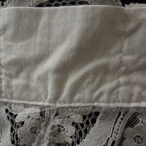 May include: Close-up of a white fabric with a lace trim. The fabric is folded and has a seam down the center.