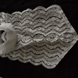 May include: White lace collar with a scalloped edge. The collar is made of delicate lace with a floral pattern.