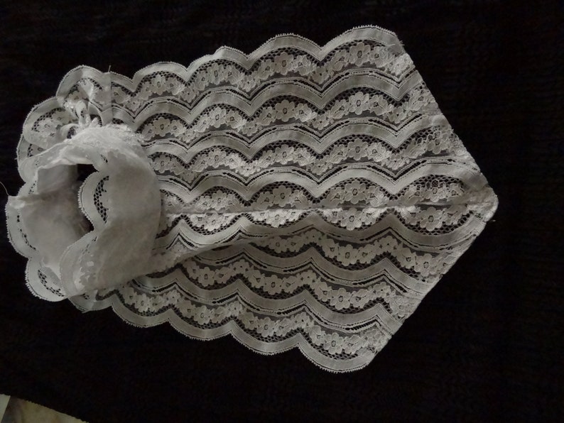 May include: White lace collar with a scalloped edge. The collar is made of delicate lace with a floral pattern.