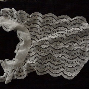 May include: White lace bodysuit with ruffled sleeves. The lace has a floral pattern and a wavy design.