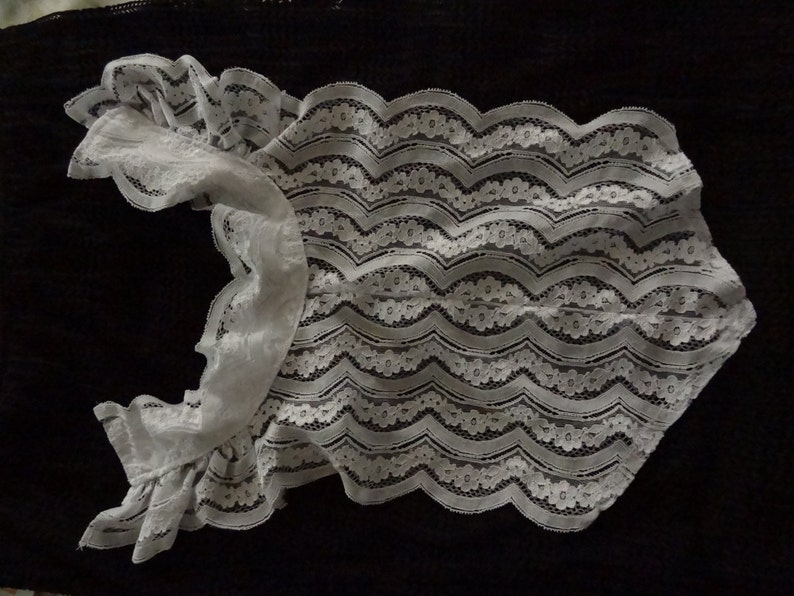 May include: White lace bodysuit with ruffled sleeves. The lace has a floral pattern and a wavy design.
