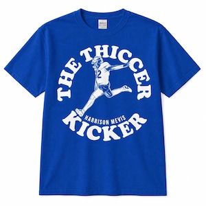 May include: A royal blue short-sleeve t-shirt featuring a white graphic of a football player in motion. The text reads THE THICCER KICKER in a circular arc with HARRISON MEVIS printed below the player. The design is centered on the chest.