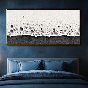 Puede incluir: Impresión artística abstracta en un marco dorado. La obra presenta un fondo blanco texturizado con formas negras en forma de burbujas en la parte inferior, que transicionan a una base negra sólida. La pieza se exhibe sobre una cama azul.