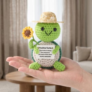 Può includere: Una piccola tartaruga all'uncinetto verde con un cappello di paglia, che tiene un girasole giallo e un cartello bianco con il testo: Positive Turtle, Tiny turtle is always here whenever you need a little cheer. YOU'RE AWESOME!