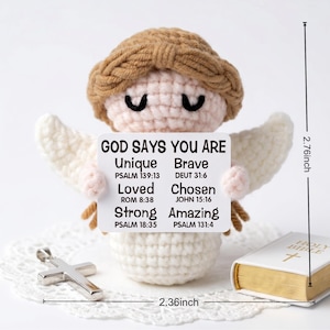 May include: A crocheted angel figurine with a brown halo and white wings holds a sign that reads "GOD SAYS YOU ARE Unique, Brave, Loved, Chosen, Strong, Amazing." A silver cross and a small book are also present. The angel is 2.76 inches tall and 2.36 inches wide.
