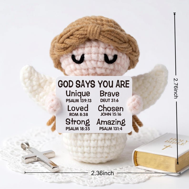 May include: A crocheted angel figurine with a brown halo and white wings holds a sign that reads "GOD SAYS YOU ARE Unique, Brave, Loved, Chosen, Strong, Amazing." A silver cross and a small book are also present. The angel is 2.76 inches tall and 2.36 inches wide.