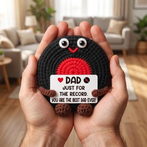 May include: A handmade crochet record with a red center and black outer ring, held in open hands. The record has googly eyes and a smiling mouth. A white sign reads "DAD JUST FOR THE RECORD. YOU ARE THE BEST DAD EVER!"