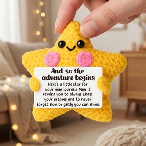 Könnte beinhalten: Ein gelbes gehäkeltes Stern-Plüschtier mit schwarzen Perlenaugen und rosa gestickten Wangen. Der Stern hält eine weiße rechteckige Karte mit dem Text: And so the adventure begins. Here's a little star for your new journey. May it remind you to always chase your dreams and to never forget how brightly you can shine.