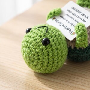May include: A handmade green crocheted turtle with black button eyes and a stitched mouth. The turtle has a tag that reads "Positive Turtle" and "You're Awesome". The turtle is a cute, whimsical item.